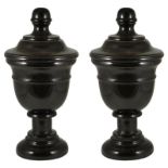 A pair of black marble lidded urns: turned marble on pedestal bases,