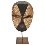 A Tribal Aduma Mask from the Gabon: Typical black and white male mask with eye slits, on stand.