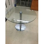 A circular glass topped table with a chrome base