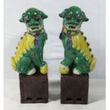 A pair of antique Chinese temple dogs sitting on aubergine coloured bases, famille verte decorated