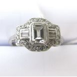 An Art Deco white metal diamond cluster ring set with a central emerald cut diamond, four small