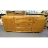 A 1960s elm Ercol sideboard having three long central drawers flanked by cupboard doors, standing on