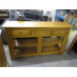 A modern light oak dresser base, with central drawers flanked by fielded drawers and shelf below