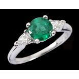 An Emerald and Diamond three stone Ring claw-set round emerald, 1.13cts, between two pear-cut