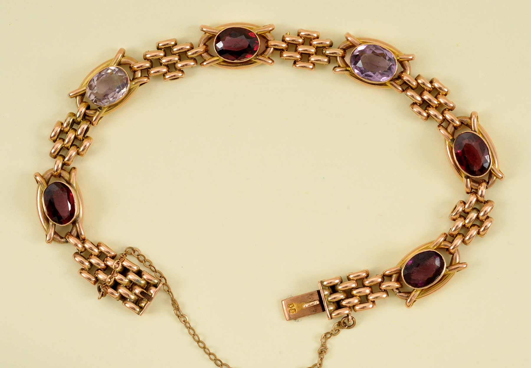 A Garnet and Amethyst Bracelet rub-over set alternating oval-cut stones in fancy links on hidden