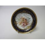 A Berlin Saucer Dish painted cherubs amongst clouds with zither, blue and gilt floral and cellular