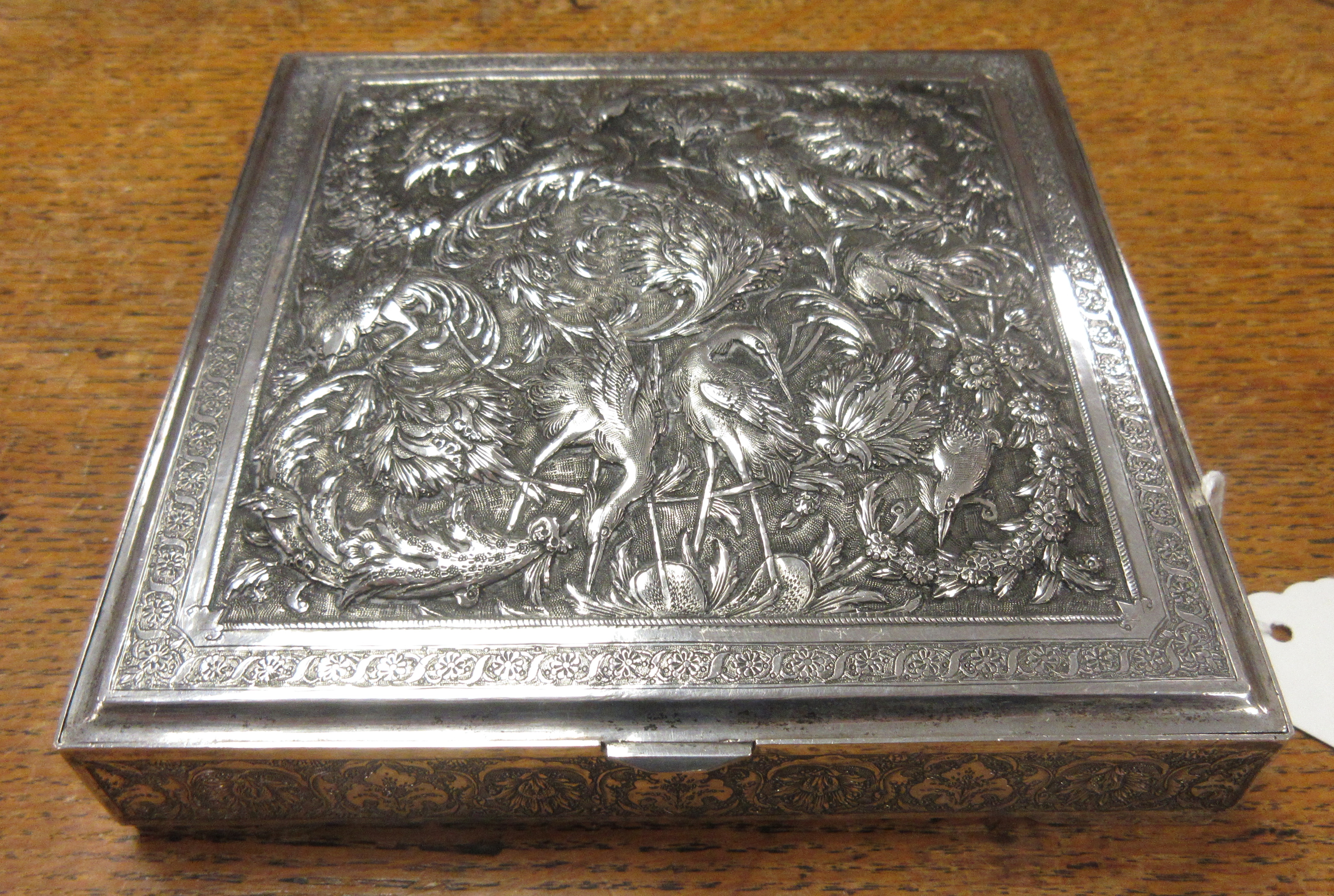 A Persian silver square Box with hinged cover finely embossed and chased with exotic birds amongst