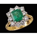 An Emerald and Diamond Cluster Ring claw-set step-cut emerald within a frame of ten brilliant-cut