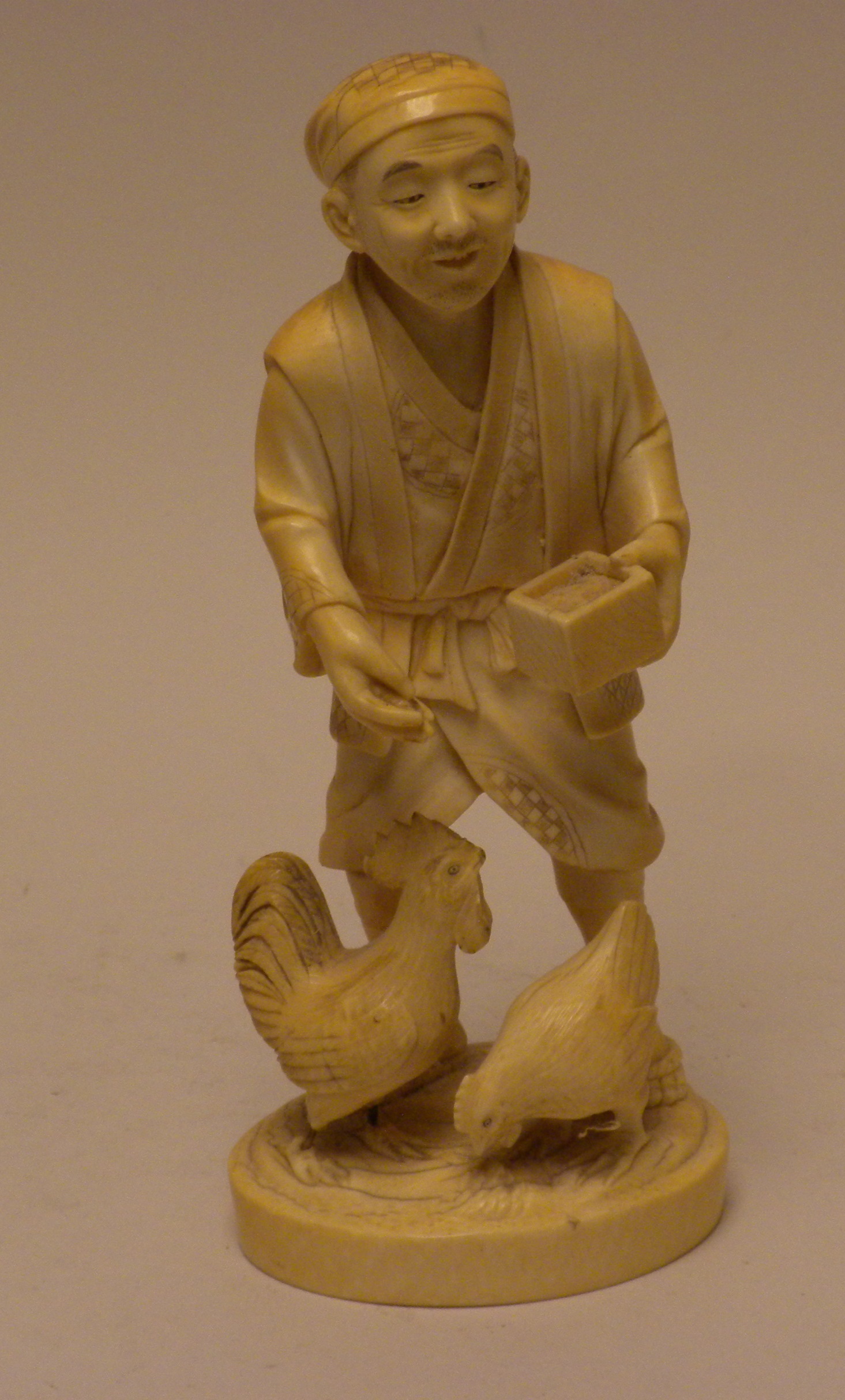 A Japanese ivory Okimono of a Chicken FarmerBy Hideyuki, Meiji Period,Standing feeding a cockerel