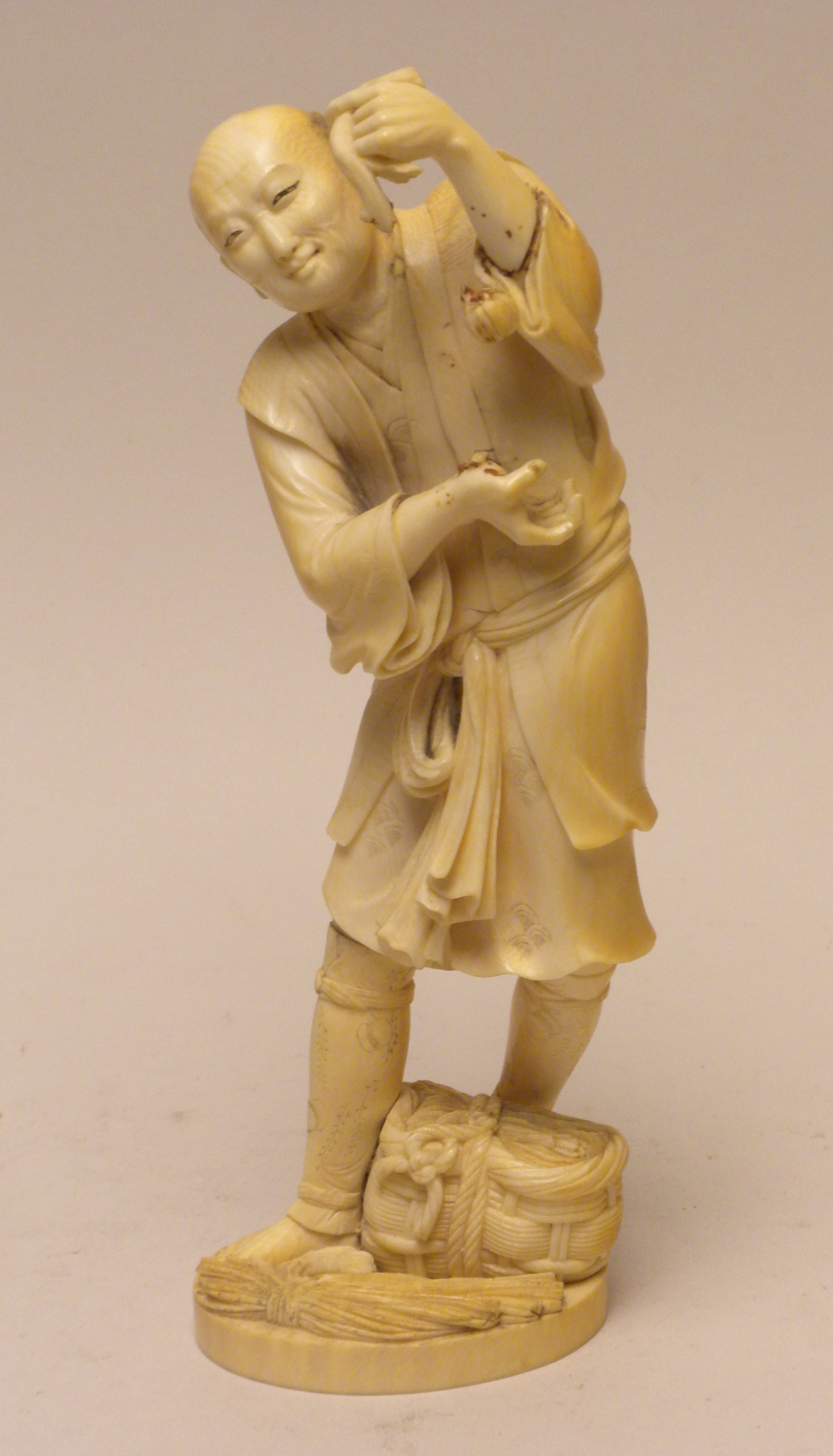 A Japanese ivory Okimono of a Farmer,Meiji PeriodStanding holding a kiku stem, a basket at his feet,