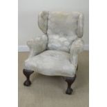 An antique Wingback Armchair with shaped front on two finely carved claw and ball feet having