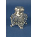 A cut glass Inkwell with floral and scroll embossed hinge lid and pen shelf, mounted upon four paw