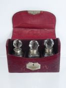 A Circa 1899 Boxed Trio of Silver Collared Scent Bottles, in the original red leather case,