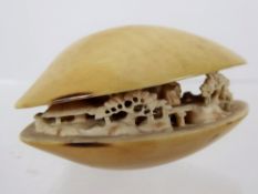 A 19th Century Japanese Ivory Netsuke, in the form of a clam, carved with figures in a garden,