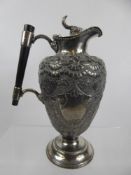 An Antique Lidded Silver Plated Claret Jug, ebony handle and embossed with floral decoration.