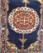 A Persian Woollen Rug, of blue and salmon colouring, depicting a floral medallion surrounded by a