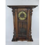 An Antique Wooden Wall Clock, with columns to either side, Roman numerals on cream enamel face,