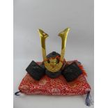 A Small Replica Japanese Samuri Dragon Cast Iron Helmet on a red and yellow silk pillow, approx 20 x