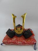 A Small Replica Japanese Samuri Dragon Cast Iron Helmet on a red and yellow silk pillow, approx 20 x