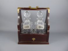 A Mahogany Tantalus with two crystal decanters, together with three silver plated liquor labels.