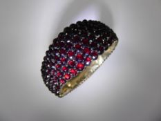 An Antique Yellow Metal and Garnet Cocktail Bangle, the bangle of domed design.