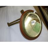 CIRCULAR BEVELLED GLASS MIRROR IN A WOODEN FRAME MOUNTED ON A BRASS ADJUSTABLE BRACKET