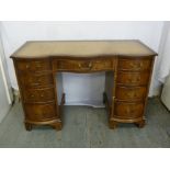 An early 20th century serpentine front kneehole desk with tooled leather top, nine drawers and brass