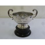 A silver rose bowl with two scroll handles on circular spreading base and carved wooden plinth,