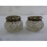 A pair of cut glass dressing table jars with pull off silver covers