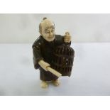 An early 20th century Japanese ivory and wood figurine of a gentleman carrying a bird cage, 8.5cm (