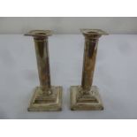 A pair of filled silver table candlesticks, tubular stems on raised square bases with reed and tie