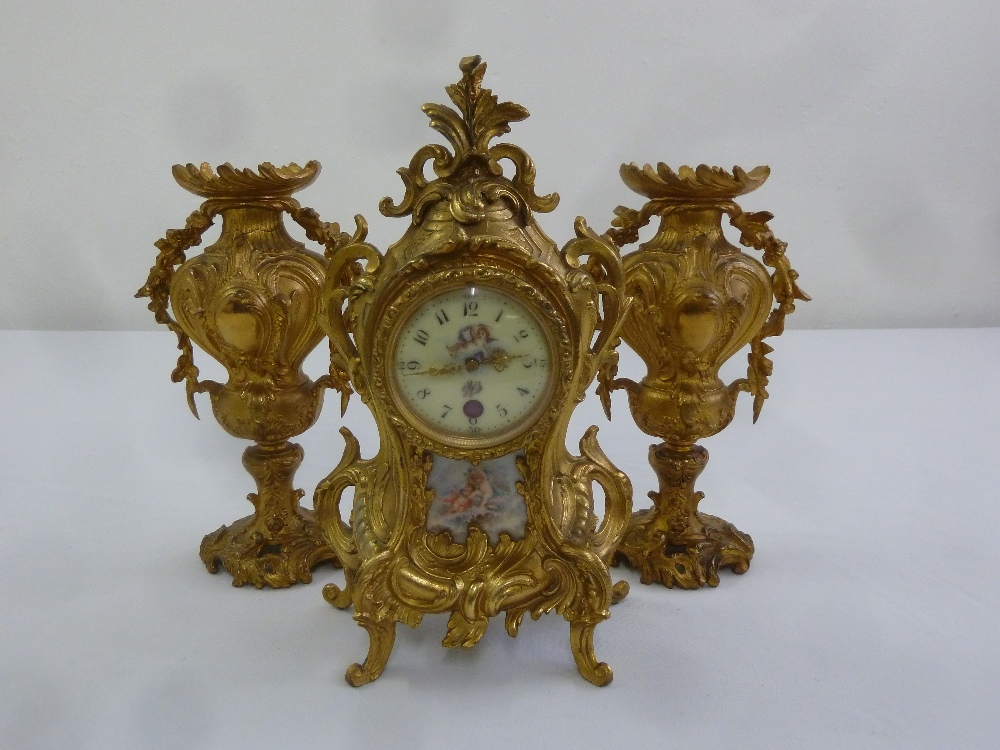 A French 19th century gilded metal mantle clock with porcelain panels and vase form garnitures