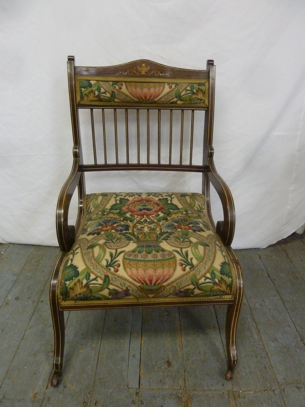 An Edwardian upholstered occasional chair with satinwood inlays and scroll legs on original castors