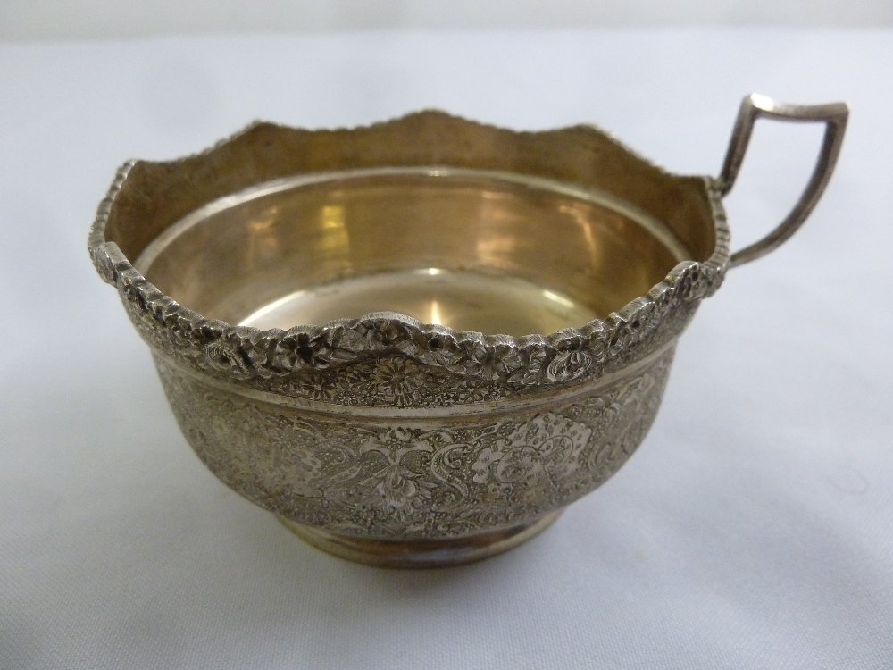 A Persian white metal cup, circular with scroll handle profusely engraved with flowers, leaves and