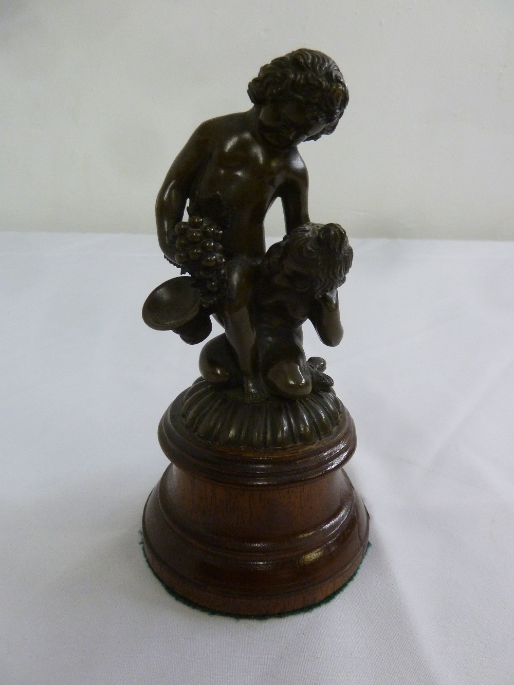 A 19th century bronze figurine of putti holding grapes on cylindrical wooden plinth, 18cm (h)