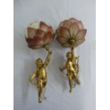 A pair of gilded metal hanging wall lights in the form of putti supporting glass shades
