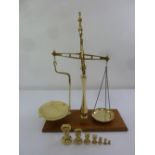 An early 20th century brass balance scale on raised wooden plinth, to include seven weights