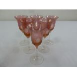 Six cranberry wine glasses etched with floral designs on raised clear glass stems