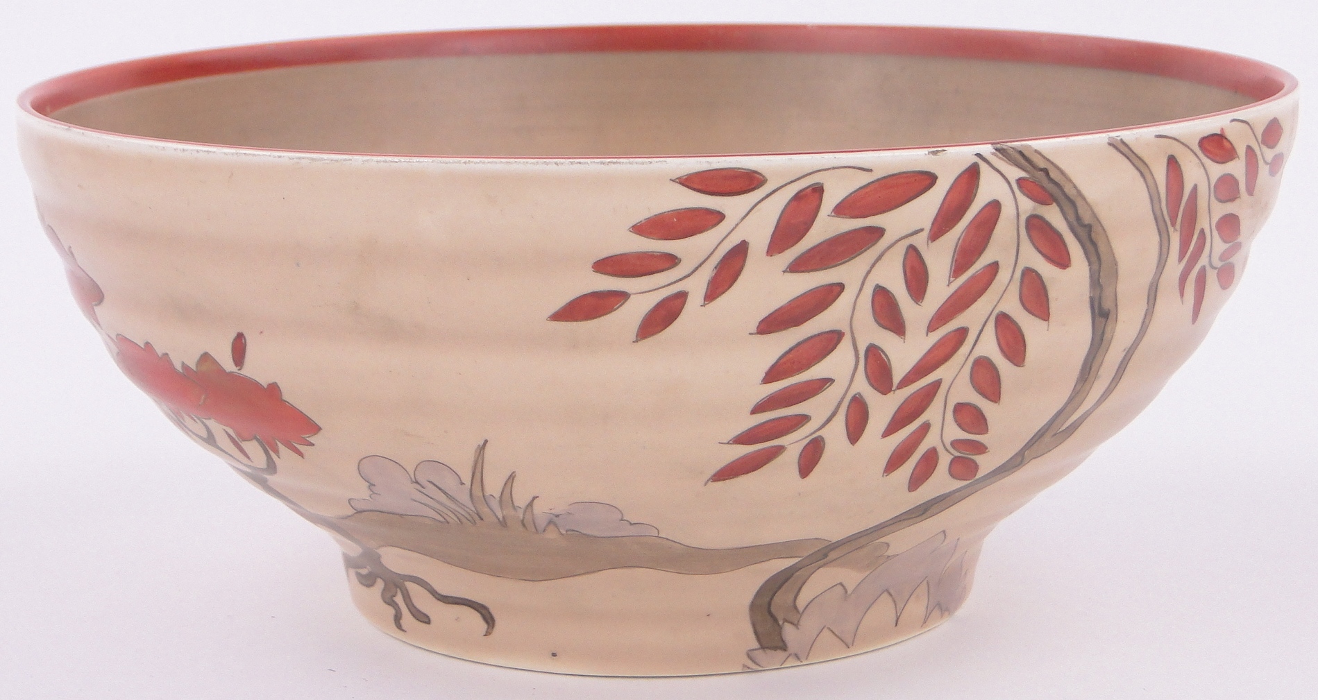 A Clarice Cliff fruit bowl with painted stylised red trees on brown ground, 9.5" diameter.