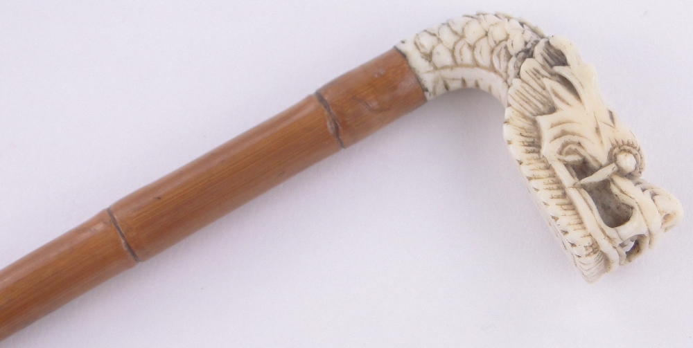 A Chinese ivory and bamboo cane circa 1900, with carved dragon's head finial, length 77cm.