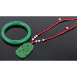 A modern Chinese relief carved jade pendant on silk cord, and a green jade bangle, (2).