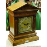 A carved oak cased mantel clock with brass dial and 2-train movement.