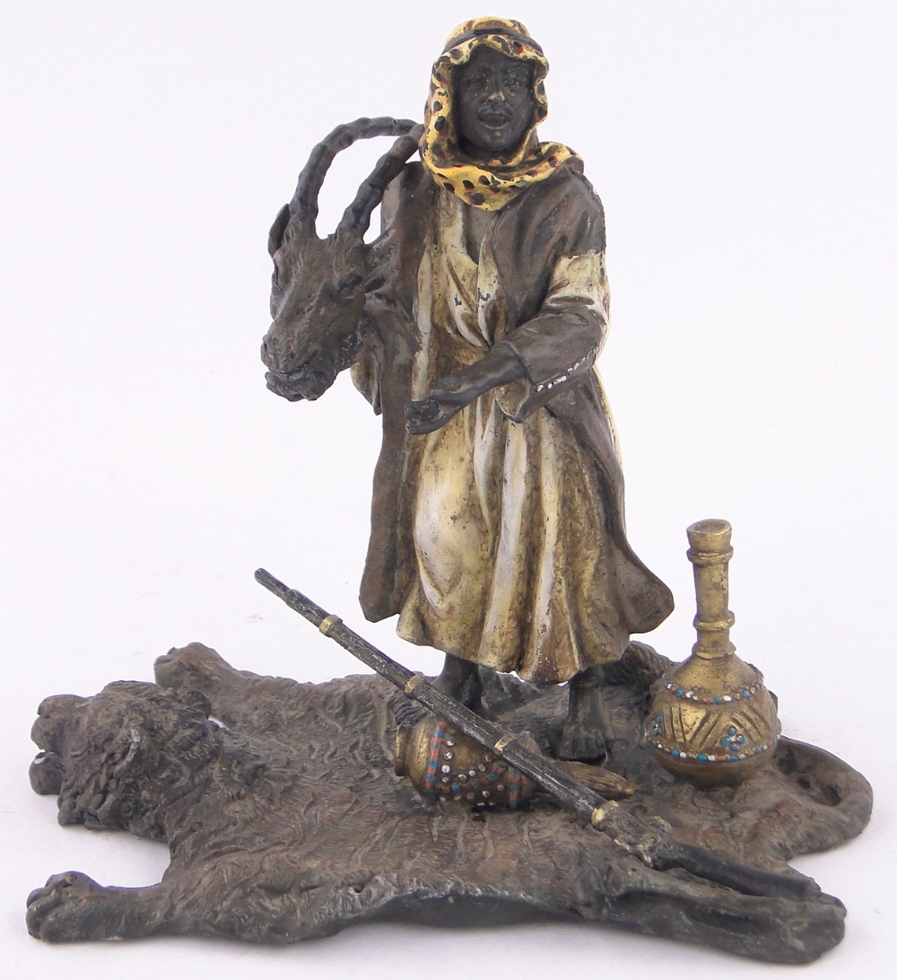 A cold painted bronze Arab huntsman standing on a tiger's skin rug, length 16cm, height 15cm.