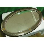 An Arts & Crafts oval wall mirror with embossed copper frame.