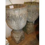A pair of embossed weathered concrete garden planters on pedestals.