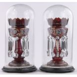 A pair of 19th century ruby glass table lustres under glass domes,