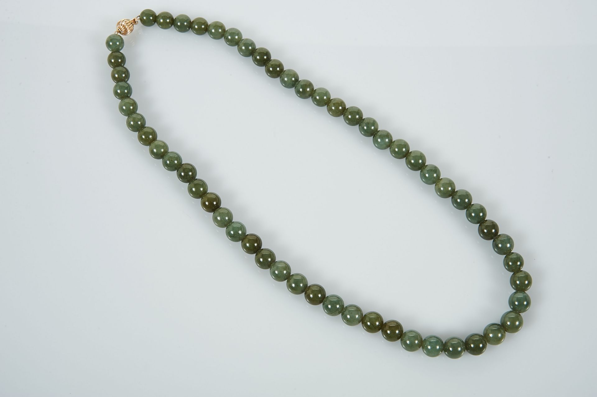 A Necklace, a string of 56 Jadeite beads (9 mm), gadrooned 14 kt. gold clasp, marked, Dim. - 57,5