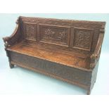 A Victorian Flemish-style dark oak settle, panelled back carved with male figures playing nine-pins,