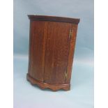 A George III oak corner cupboard, two shaped shelves enclosed by a pair of bow doors with brass H-