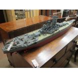 A model radio-controlled battleship, with numerous gun turrets, stern as an aircraft carrier, four-